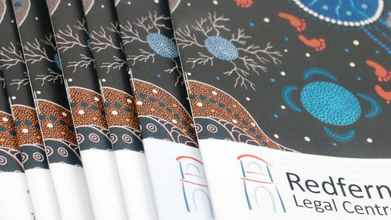 reports stread out on a table with a black green and orange Aboriginal design on the cover and the words RedFern Legal Centre on the cover