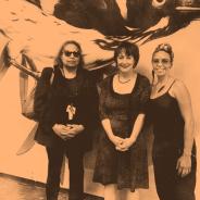 three diverse women stand together, two on left have hands clasped, two on right are are smiling