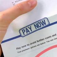 A close up of a hand holding a bill that reads pay now in large blue type