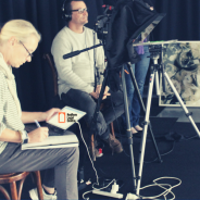 RLC in the Media - behind the scenes filming a new piece. A journalist sits preparing whilst a camera man adjusts levels on a camera.