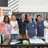 Group of volunteers stand in front of a banner that reads Redfern. Legal Centre