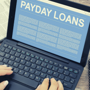 Hands typing on a laptop - the screen is blue and white and reads Payday Loans