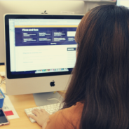 Student with long dark hair  sits in front of a a computer