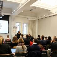 Group of people watching a woman delivering a PowerPoint presentation