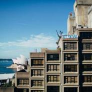 Exterior shot of housing commission apartments against Sydney skyline, with a banner reading "Not For Sale" across rooftop 