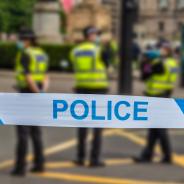 Blurred image of police standing on a road behind a strip of blue and white police tape