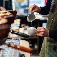 Close up a barista hands pouring milk from a silver jug into a cup ofcoffee