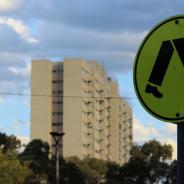 two apartment block in the distance against a blue cloudy sky. In the foreground is a black and yellow zebra crossing sign.